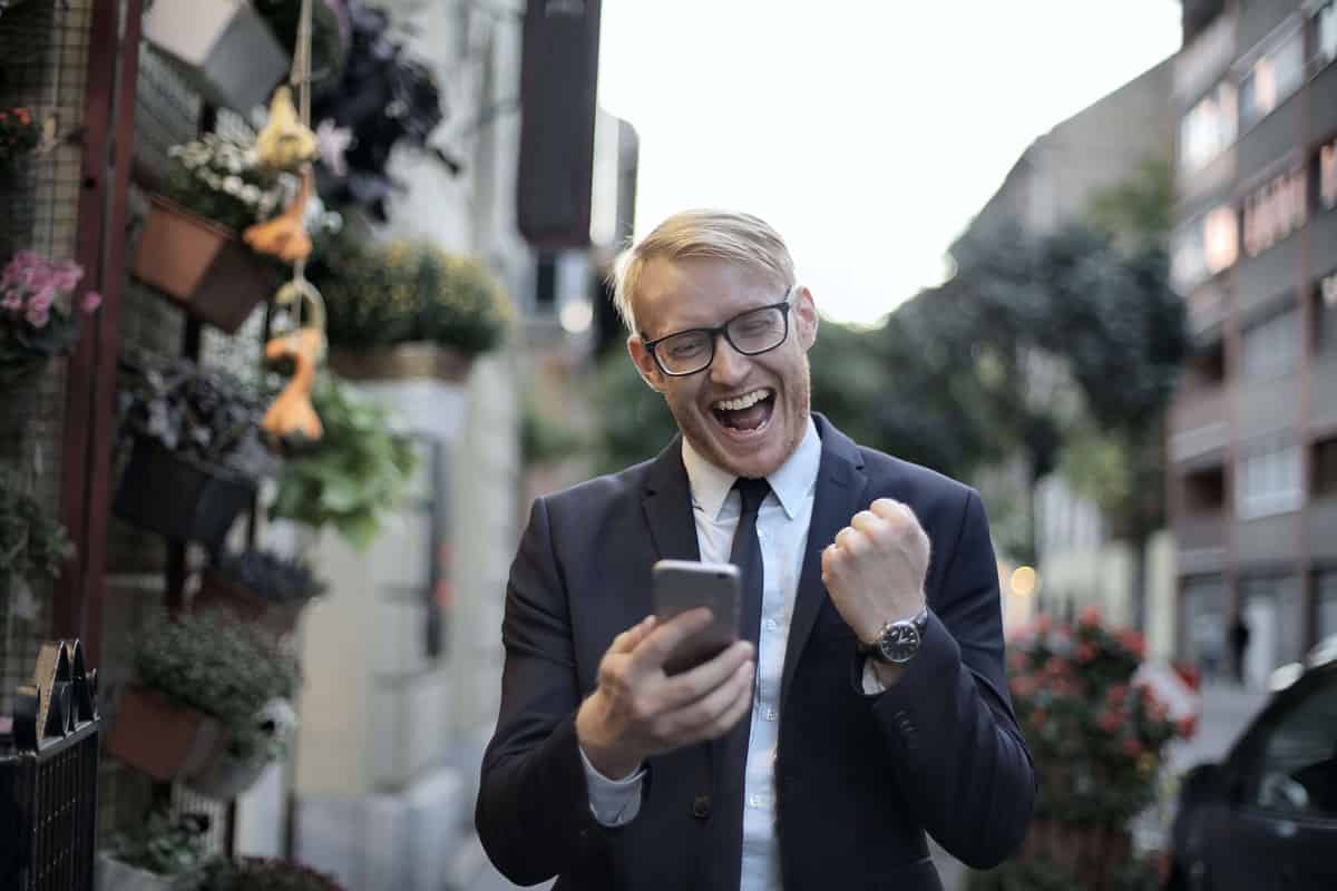 A man in a suit looks at a phone and appears excited to see how he is being acknowledge for his thought leadership. 