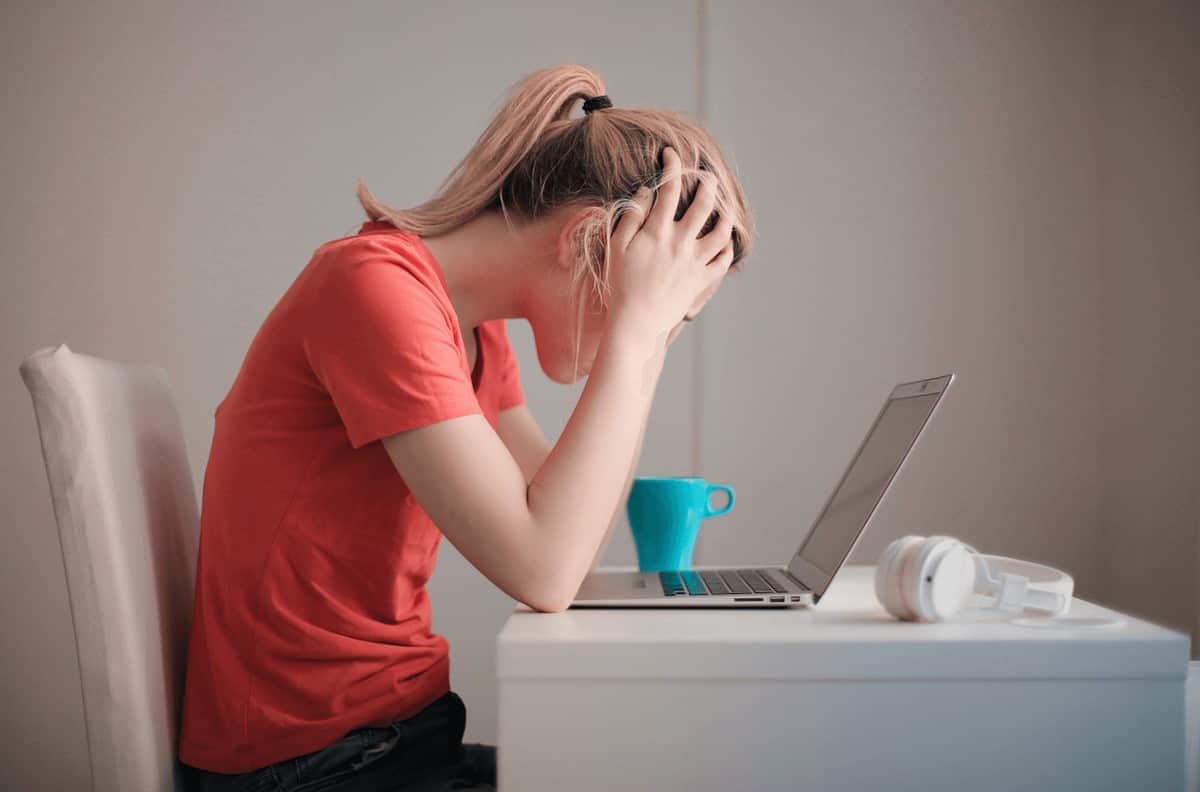 A woman holds her head in her hands as she sits before a laptop computer. Are you using a lead magnet to connect and serve her?

